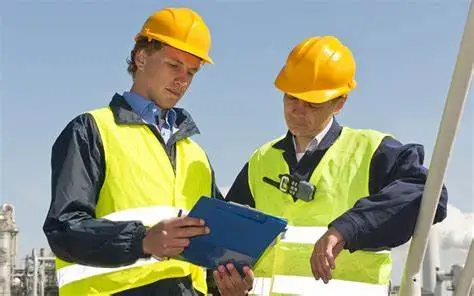 Trabajadores en un sitio industrial con cascos de seguridad, uno sosteniendo un portapapeles.